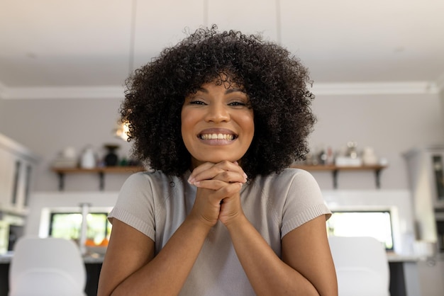 Portret van opgewonden, gelukkige biraciale vrouw met afro die thuis zit en een videogesprek maakt en glimlacht