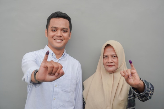 Portret van opgewonden Indonesische familie met de kleine vinger gedompeld in paarse inkt na het stemmen voor de algemene verkiezingen of Pemilu voor president en regering geïsoleerde grijze achtergrond