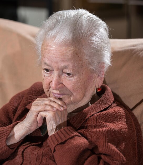 Portret van oude grijsharige trieste vrouw thuis Zieke depressieve oude vrouw