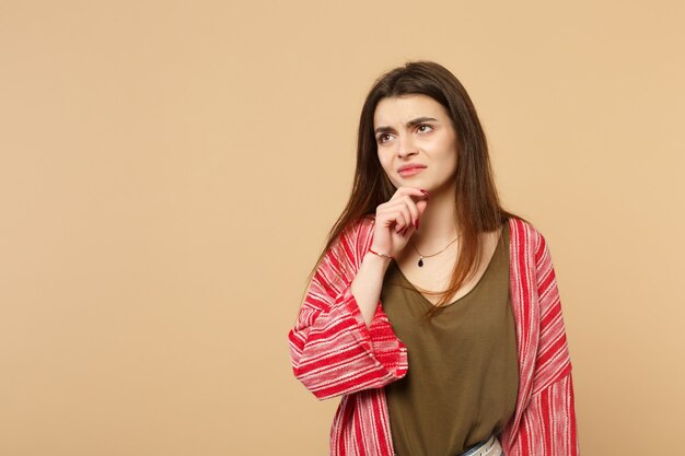 Portret van overstuur peinzende jonge vrouw in casual kleding opzoeken, hand prop op kin geïsoleerd op pastel beige muur achtergrond. Mensen oprechte emoties, lifestyle concept. Bespotten kopie ruimte.