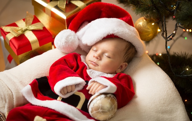 Portret van pasgeboren babyjongen in kerstmankleren die onder de kerstboom liggen