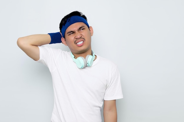 Portret van peinzende jonge aziatische sportman in blauwe hoofdband en sportkleding witte t-shirt met koptelefoon vraag me af over vraag geïsoleerd op witte achtergrond workout sport concept