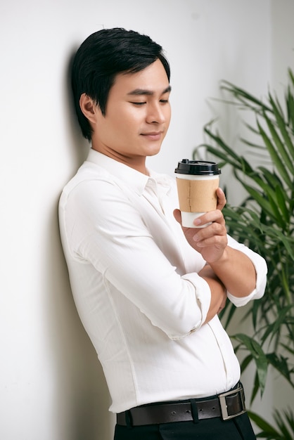 Portret van peinzende jonge vietnamese zakenman met kopje koffie leunend op de muur