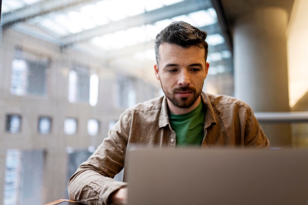 Portret van peinzende knappe Latijnse student die werkt bij een laptop freelancer die in een modern kantoor werkt