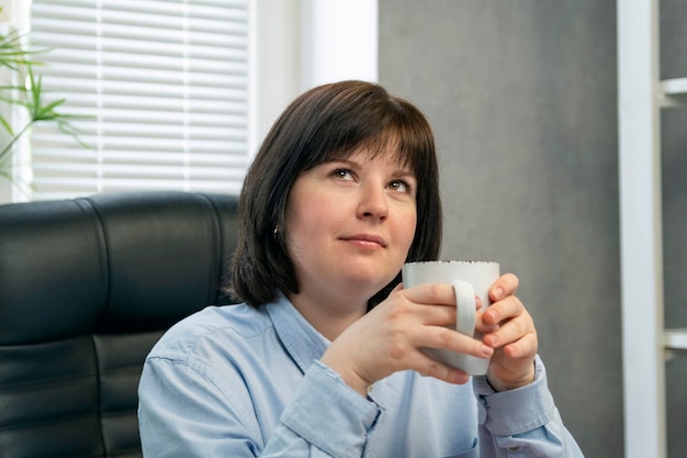 Portret van peinzende vrouw met kopje koffie in haar handen. Mooi donkerbruin meisje. Lunchpauze. Koffiepauze.