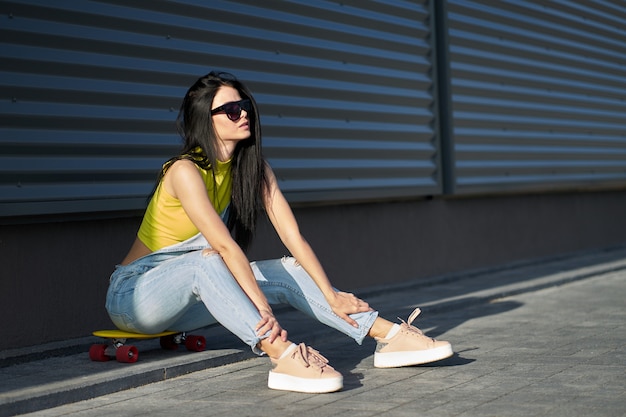 Portret van positief jong aantrekkelijk meisje die gele hoogste en jeans met geel skateboard dragen.
