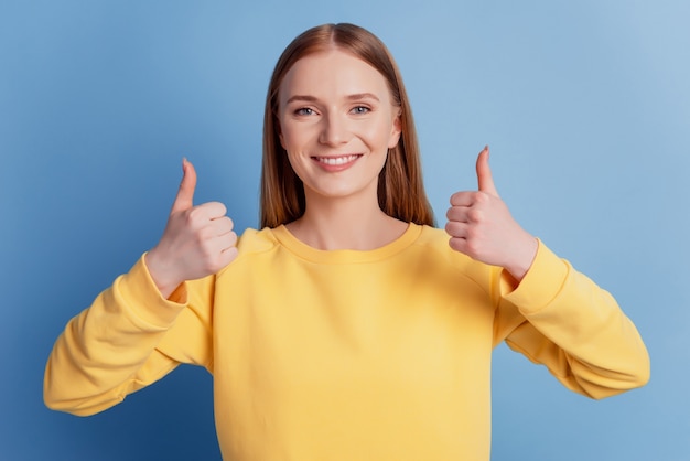 Portret van positieve aardige dame steekt duimen omhoog glanzende glimlach eens besluit op blauwe achtergrond