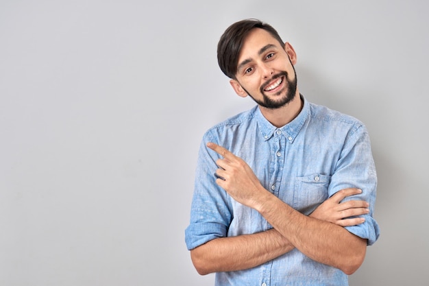 Portret van positieve blanke jonge man glimlachend en wijzend met vinger naar lege ruimte op witte studio achtergrond
