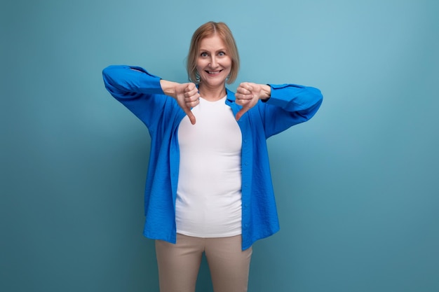 Portret van positieve blonde vrouw in blauw stijlvol shirt met afkeer op studioachtergrond