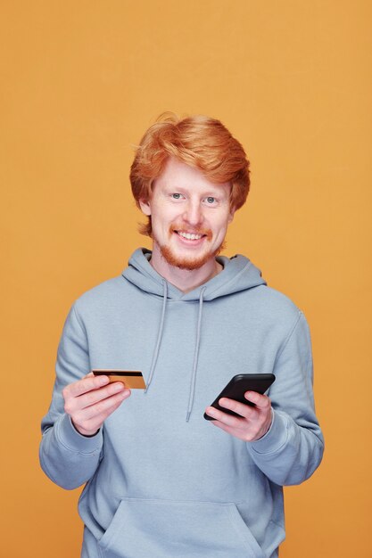 Portret van positieve jonge roodharige man in hoodie tegen oranje muur