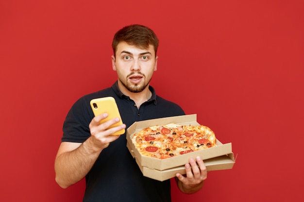 Portret van positieve man staat en opent doos met heerlijke verse pizza