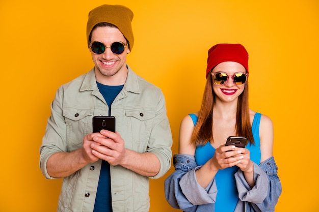 Portret van positieve twee mensen studenten bloggers man vrouw gebruik smartphone sms'en typen sociale media dragen zonnebril shirt denim jeans jasje geïsoleerd heldere glans kleur achtergrond
