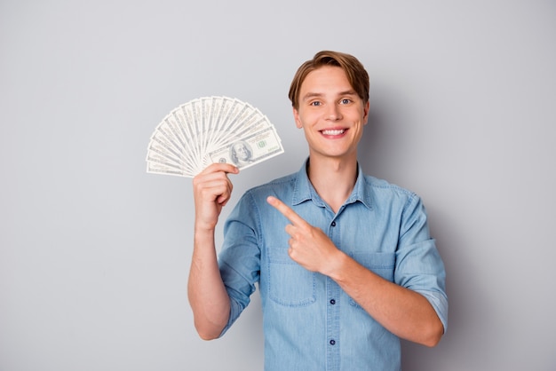 Portret van positieve vrolijke kerel houden geld fan punt wijsvinger aanbevelen