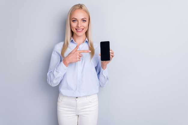 Portret van positieve vrolijke promotor meisje houdt nieuwe smartphoneapparaat wijsvinger