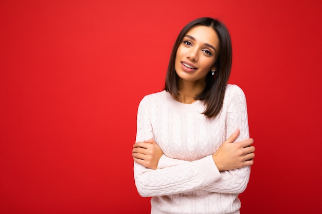 Portret van positieve vrolijke schattige lachende jonge brunette vrouw in casual trui geïsoleerd op rode achtergrond met kopie ruimte.