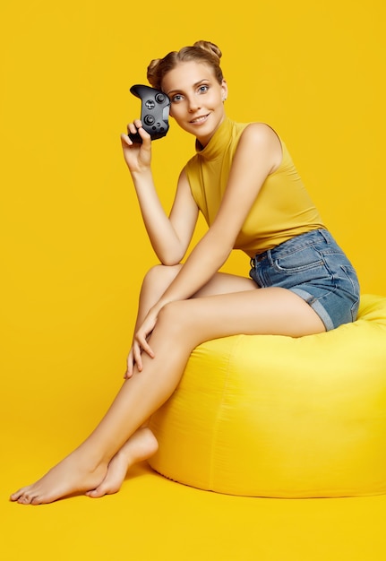 Portret van prachtige gelukkige blonde gamer meisje spelen van videogames met behulp van joystick op gele muur