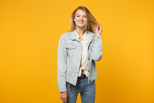 Portret van prachtige lachende jonge vrouw in denim casual kleding permanent en kijken camera geïsoleerd op fel geel oranje muur achtergrond in studio. Mensen levensstijl concept. Bespotten kopie ruimte.