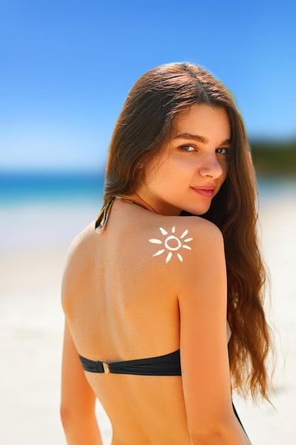 Portret van prachtige vrouw in bikini met de getekende zon op een schouder op het strand