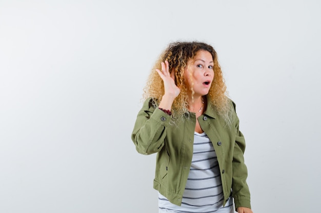 Foto portret van prachtige vrouw met hand achter oor te horen in groene jas, shirt en op zoek gericht vooraanzicht