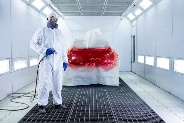 Portret van professionele autoschilder die het schilderen kanon houden en zich door auto in de kamer bevindt.