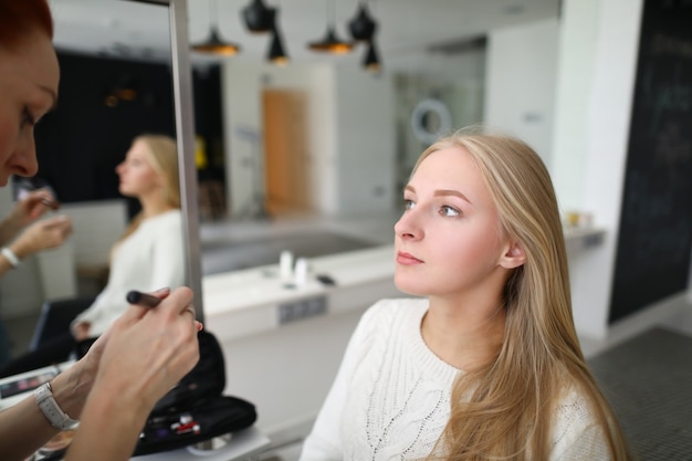 Portret van professionele make-up artiest lippenstift met speciale apparatuur toe te passen. jonge mooie vrouw in schoonheidssalon. roodharige specialist met palet met oogschaduw. mua concept