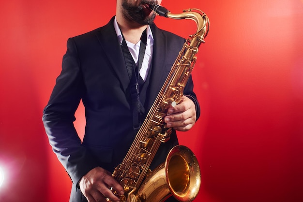 Portret van professionele muzikant saxofonist man in pak speelt jazzmuziek op saxofoon, rode achtergrond in een fotostudio