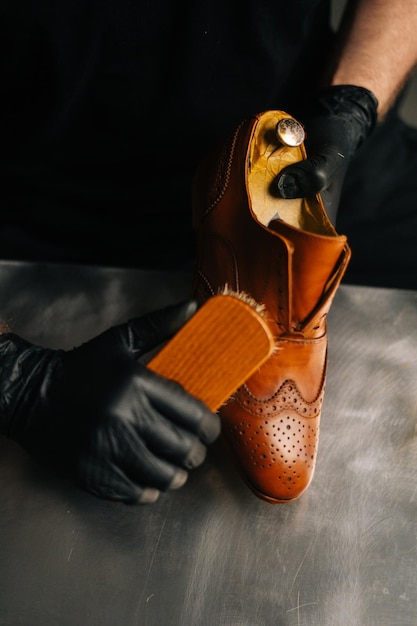 Portret van professionele schoenmaker in zwarte handschoenen die lichtbruine leren schoenen polijsten met borstel