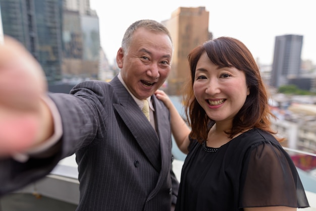 Portret van rijpe Japanse zakenman en rijpe Japanse vrouw die de stad Bangkok verkennen