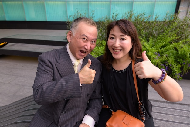 Portret van rijpe Japanse zakenman en rijpe Japanse vrouw die de stad Bangkok verkennen