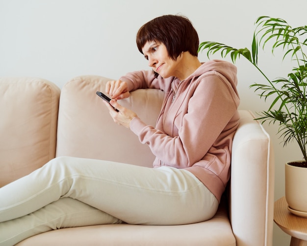 Portret van rijpe vrouw die op mobiele telefoon met verrassing en alarmverwarring en frons kijkt