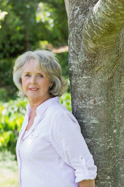 Portret van rijpe vrouw die tegen boomboomstam leunen