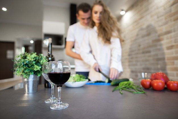 Portret van romantisch paar in de keuken thuis. Blondevrouw met de lange komkommer van haarplakken. Een man die een vrouw aan de zijkant knuffelt