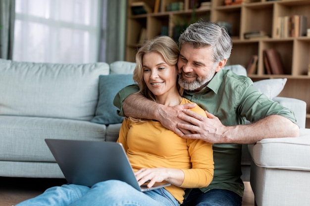 Portret van romantische echtgenoten van middelbare leeftijd ontspannen met laptop thuis