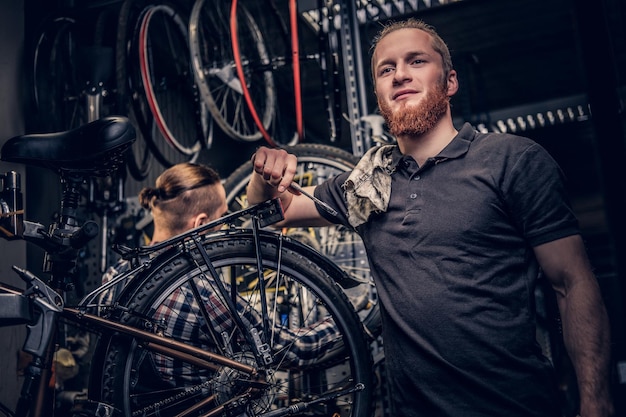 Portret van rood hoofd bebaarde fietsenmaker in een werkplaats met fietsonderdelen en wiel op een achtergrond.