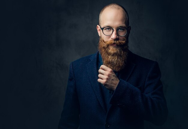 Portret van roodharige bebaarde man in brillen gekleed in een elegante wollen pak over grijze achtergrond.