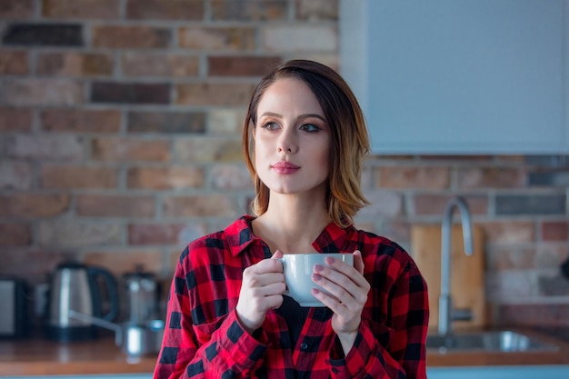 Portret van roodharige vrouw met kopje koffie of thee in de keuken in de ochtendtijd