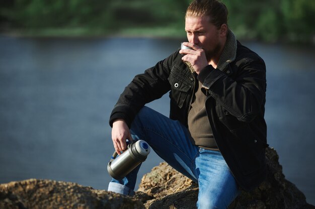 Portret van rustende bergbeklimmer en het drinken van hete thee of koffie bij meer. Concept van ontspanning en reizen in de natuur