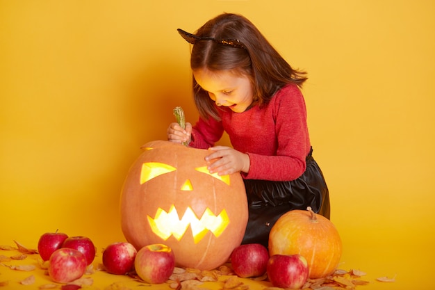 Portret van schattig grappig Kaukasische meisje gekleed met gele herfstbladeren, appels en pompoenen voor Halloween