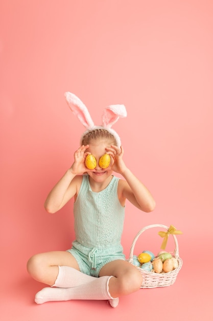 Portret van schattig lachend meisje met konijnenoren en paaseieren op roze achtergrond