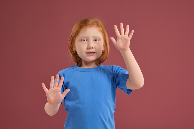 Portret van schattig roodharig emotioneel klein meisje op rode achtergrond