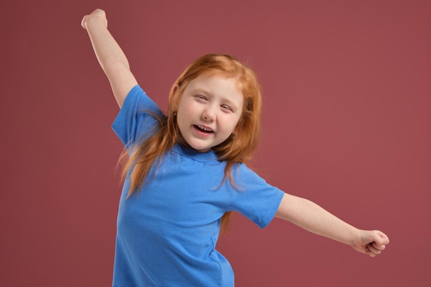 Portret van schattig roodharig emotioneel klein meisje op rode achtergrond