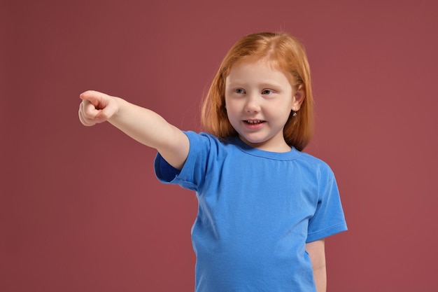 Portret van schattig roodharig emotioneel klein meisje op rode achtergrond