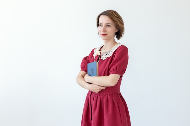 Portret van schattige glimlachende bescheiden vrouw in jurk klassiek boek in handen op witte muur te houden. Concept van liefhebbers van geschiedenis en klassiekers.