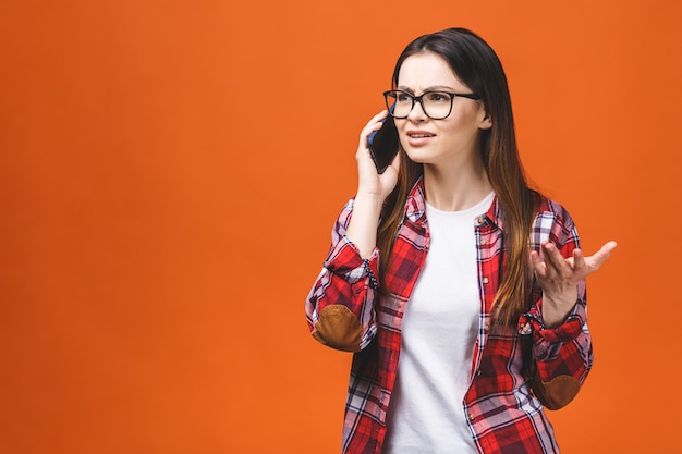 Portret van schattige jonge vrolijke vrouw met trendy kapsel casual dragen, praten op mobiele telefoon geïsoleerd op oranje achtergrond.