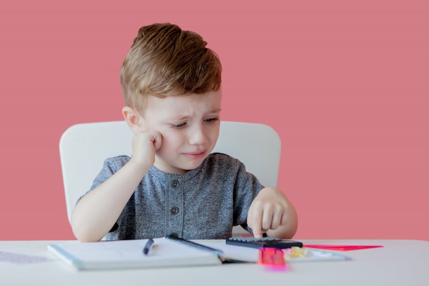 Portret van schattige jongen jongen thuis huiswerk maken. Weinig geconcentreerd kind dat met kleurrijk potlood schrijft, binnen.