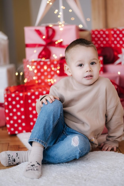 Portret van schattige kleine jongen thuis tijdens de wintervakantie kerstboom en veel cadeautjes