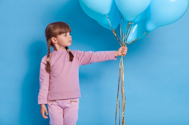 Portret van schattige kleuter poseren tegen blauwe muur met ballonnen