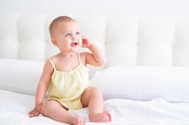 portret van schattige lachende babymeisje in gele bodysuit op wit beddengoed. Gezond pasgeboren kind