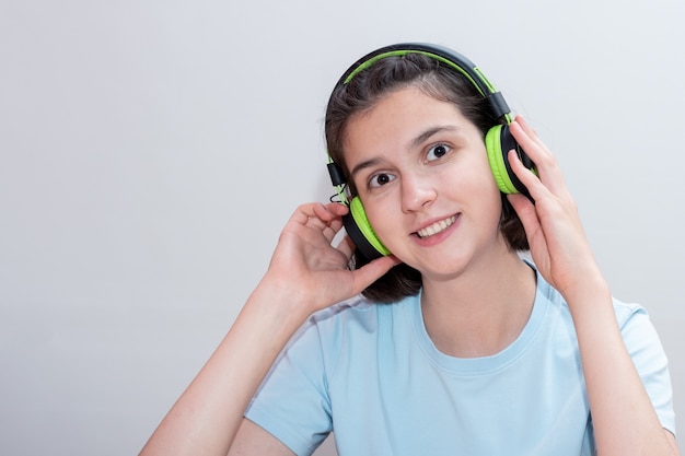 Portret van schattige lachende positieve meisje tiener luisteren naar muziek in groene koptelefoon op wit