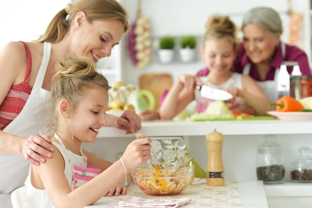 Portret van schattige meisjes met moeder die heerlijke verse salade in de keuken bereiden